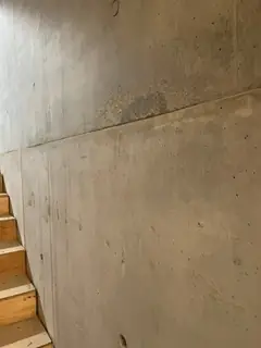 Wand neben einer Holztreppe mit waagerechter Fuge, darüber ein heller, körniger Fleck