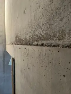 Betonierfuge mit körnigem, dunklem Band darüber, links unten ein blauer Streifen an der Wandkante