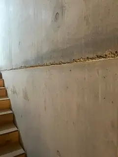 Betonierfuge mit rostbraunem, rauem Rand an einer Wand neben einer Holztreppe