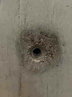 Spindelloch mit krümeligem, ausgebrochenem Ring und dunklem Hof, darüber eine senkrechte feine Fuge