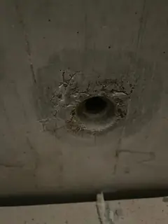 Spindelloch mit dunklem Hof und feinen Rissen am oberen Rand, unten eine Schalungskante