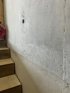 Betonwand neben einer Holztreppe mit senkrechter Fuge, einem Ankerloch und schräg abfallendem Anschluss
