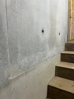 Betonwand zwischen zwei Holztreppen mit zwei Ankerlöchern und hellem, schräg verlaufendem Übergang