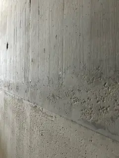 Betonwand mit waagerechter Fuge, rechts daneben viele kleine, körnige Ausbrüche in der Oberfläche
