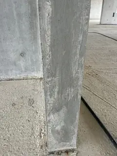 Kante einer Betonstütze mit streifiger, hellgrauer Oberfläche im Rohbau, rechts ein Estrichboden mit Kabel