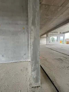 Betonstütze mit streifiger Oberfläche im offenen Erdgeschoss, im Hintergrund eine Kassettendecke und Fensterfront