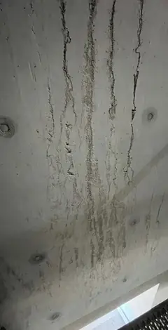 Mehrere senkrechte Auswaschungen mit Rissen und rauen Rinnen auf einer Sichtbetonfläche mit zwei Ankerlöchern