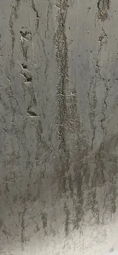 Senkrechte, ausgewaschene Rinne mit faserigen Kiesresten und weiteren Streifen daneben im Sichtbeton