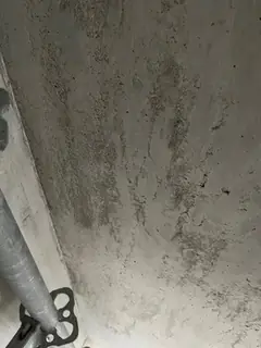 Sichtbeton mit senkrechten Auswaschungen, links ein schräges Stahlrohr mit schwarzer Klemme