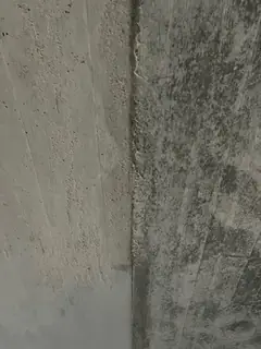 Senkrechte Kante zwischen heller und dunkel gefleckter Betonfläche, unten eine glatte graue Zone