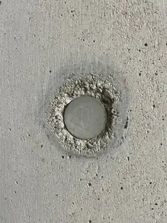 Grauer Stopfen in einem Ring aus ausgebrochenem, krümeligem Beton, die Fläche zeigt viele Poren
