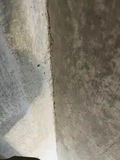Betonecke mit stark gefleckter, dunkler und heller Oberfläche, links gelblich schimmernde Bereiche