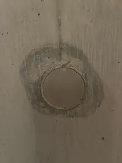 Runder Stopfen mit schmalem Randspalt, umgeben von einem unregelmäßigen, dunklen Hof auf glattem Beton