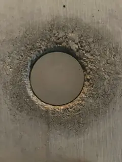 Dunkelgrauer Stopfen in einer tiefen Randfuge, ringsum eine grobe, sandig-dunkle Zone