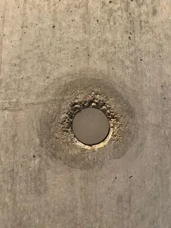 Sehr kleiner Stopfen mit krümeligem Rand und rundem dunklem Hof, schwach gemaserte Betonfläche