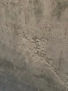Diagonales Band aus rauen, krustigen Ausbrüchen in der Betonfläche, darüber dunkle Flecken