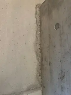 Senkrechte Betonkante mit unregelmäßig ausgebrochenem Streifen, rechts an der Stütze ein kleiner Ankerkonus