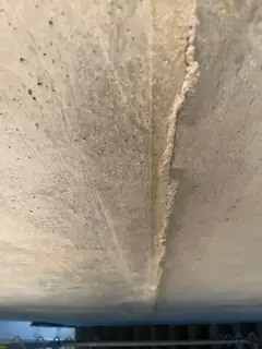 Untersicht einer Betonkante mit hell ausgebrochenem Saum und strahlenförmigen Spuren, unten ein Gerüst