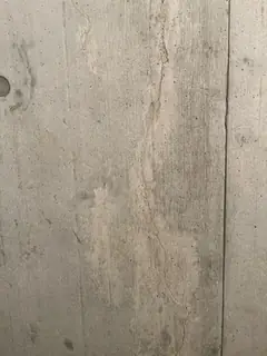 Betonfläche mit wellig verlaufender heller Zone aus Kiesnestern und einem Ankerloch am linken Rand