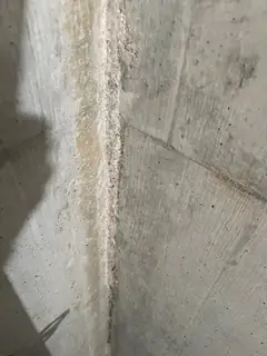 Betonkante mit krustig-gelblichem Saum an der Ecke, links ein langer Schatten auf der Fläche