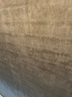 Betonwand mit waagerechten braunen und dunklen Bändern, unten eine blaue Fläche