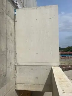 Außenansicht eines Sichtbetonbaukörpers mit vorspringendem Wandteil, im Hintergrund Himmel und Landschaft