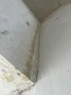 Innenecke zweier Betonteile mit feinem Riss entlang der Ecke und gelblichen Verfärbungen links