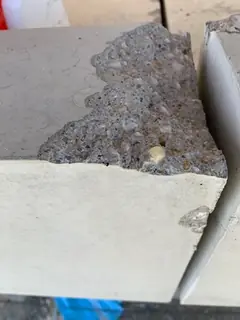Große Abplatzung an der oberen Ecke einer Betonplatte, das grobe Korn liegt offen, rechts ein Spalt