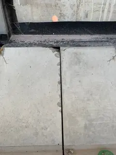 Zwei Betonplatten mit senkrechter Fuge unter einem Fensterrahmen, an der Fuge kleine Randausbrüche