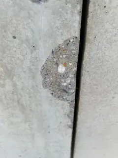 Abplatzung mit freiliegendem Korn an einer Plattenkante neben einer tiefen, schwarzen Fuge