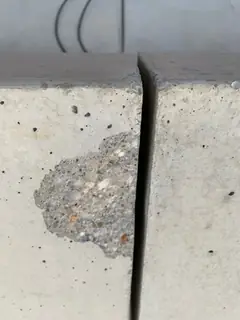 Ausgebrochene Stelle an einer Plattenecke mit grobem Korn, rechts eine schmale Fuge zur Nachbarplatte