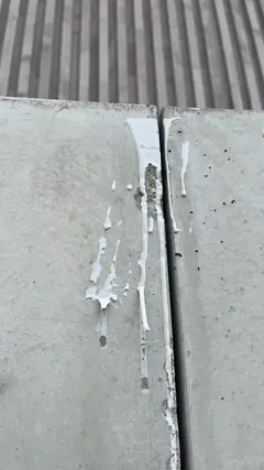 Weiße Läufer aus Fugenmasse an einer Plattenfuge, daneben zwei kleine Löcher in der Betonfläche