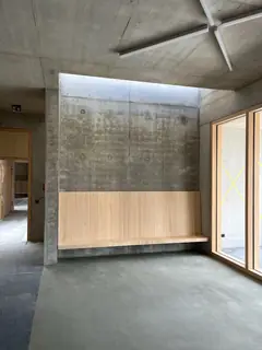 Innenraum mit Betonwand über einer Holzverkleidung, oben eine Lichtöffnung, unten ein Estrichboden