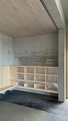 Innenraum mit Betonwand, helle Holzfächer in Folie und einer Holzdecke, unten ein Estrichboden