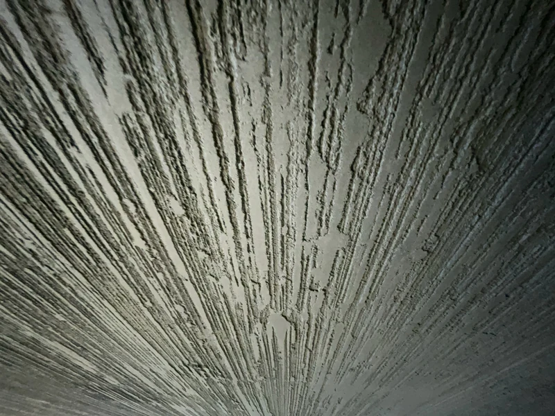 Nahaufnahme von unten auf Grate und kleine Abrisse in der von Hand gezogenen Kalkstruktur einer schwarzen Wand