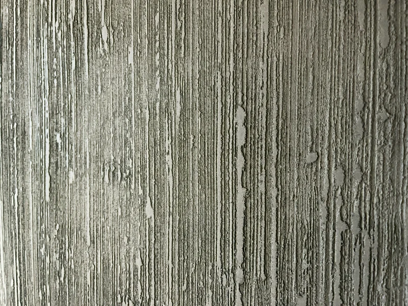Grate fangen das Licht, Rillen bleiben dunkel: Nahaufnahme einer Kalkstruktur an einer schwarzen Wohnraumwand