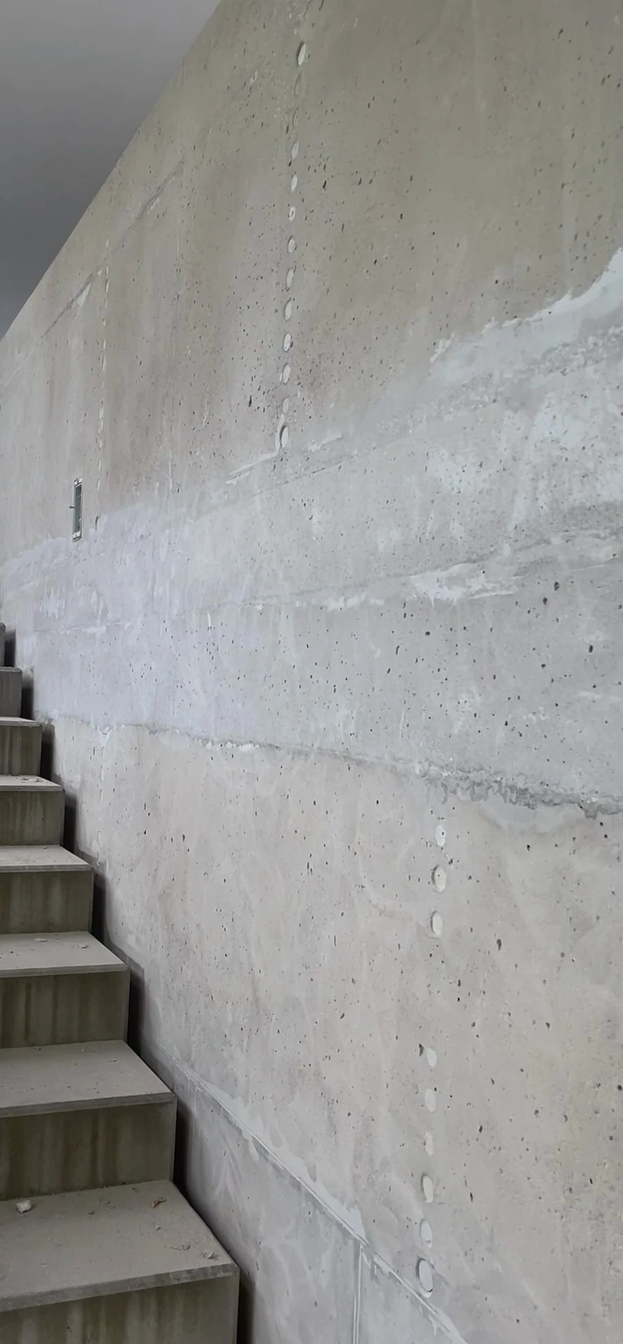Treppenwand, von unten fotografiert, Geschliffen: Abgeschliffene Betonwand neben einer Treppe, roher Beton mit Schalungsfugen, vor der Beschichtung