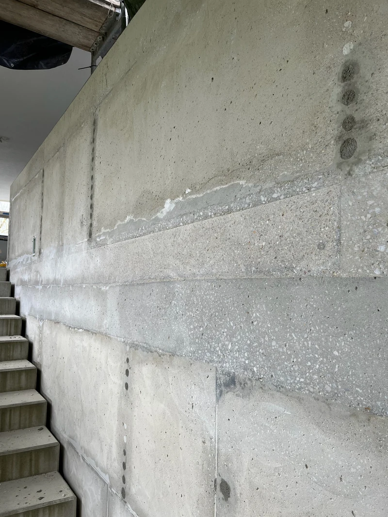 Treppenwand, von unten fotografiert, Konuslöcher zu: Abgeschliffene Betonwand ohne Farbe mit Schalungskanten und grob geschlossenen Konuslöchern, Hohenstein-Ernstthal