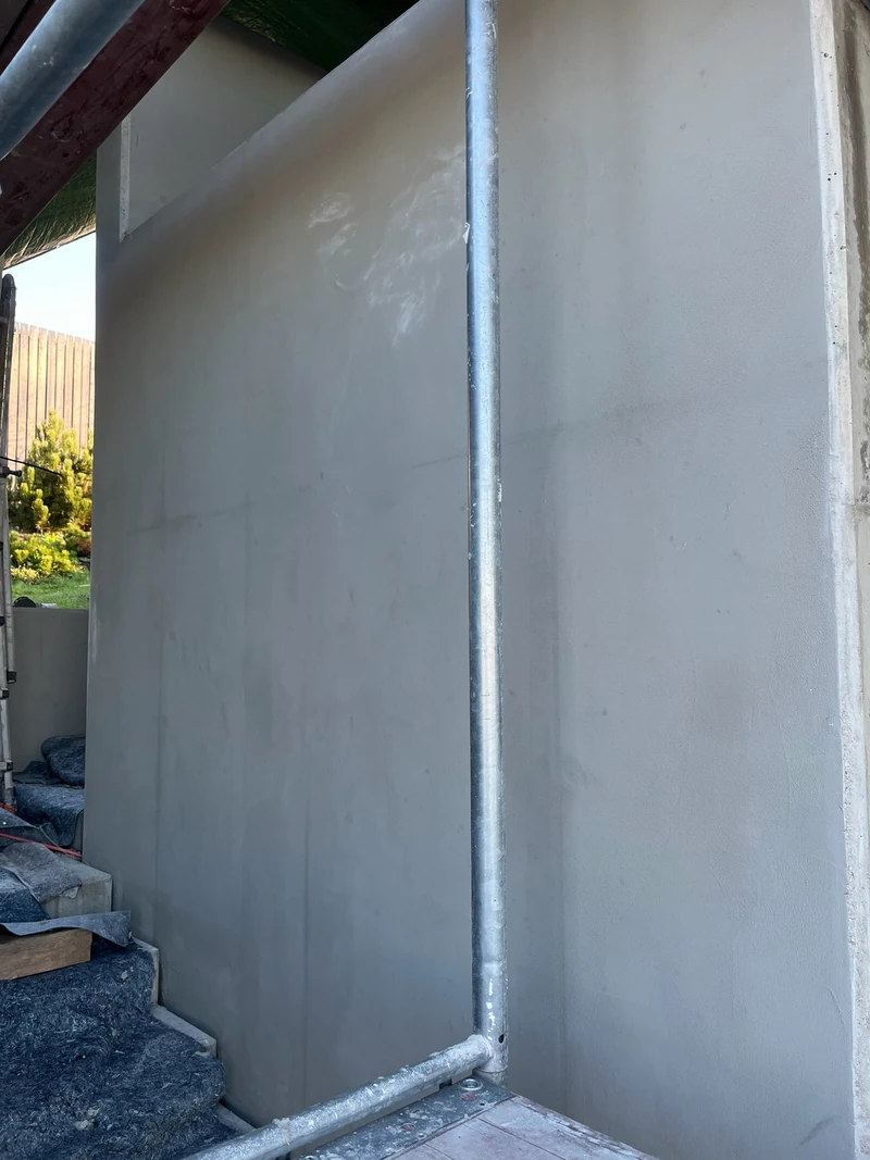 Betonwand nach der ersten Grundspachtel, gleichmäßig graue Fläche neben dem Gerüst