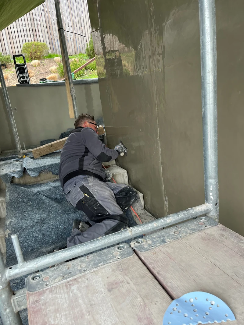 Handwerker kniet am Gerüst und glättet die Schalbetonfolie auf einer frisch beschichteten Wand