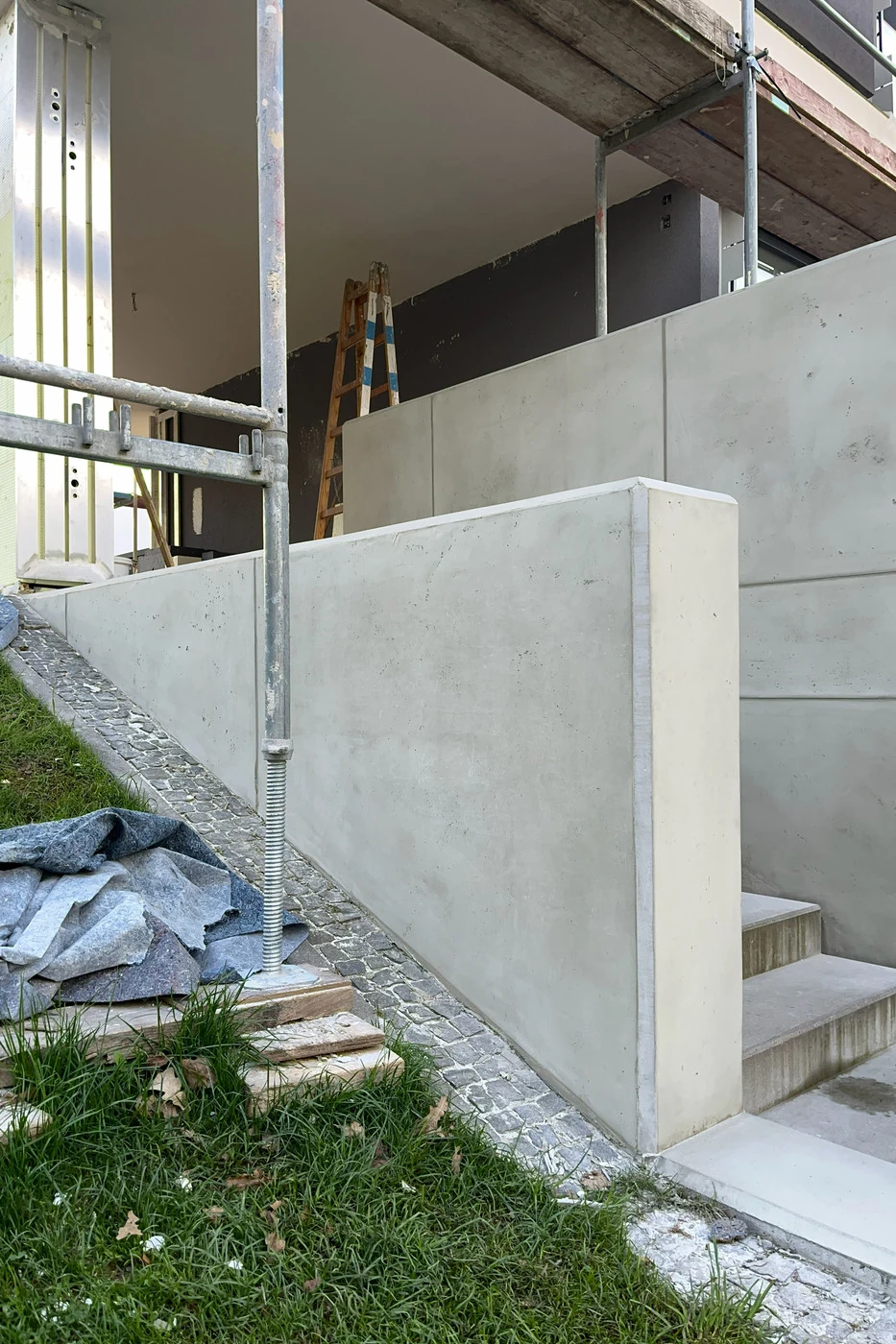 Niedrige Mauer und große Wand in Schalbetonoptik an einem Treppenabgang im Garten