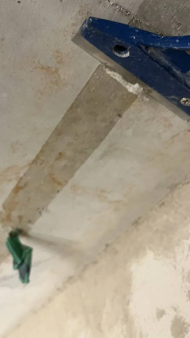 Ein Glasschaber löst das Klebeband von der Betondecke.