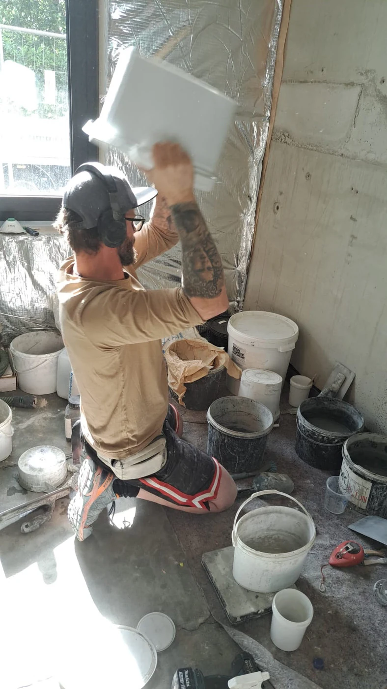 Handwerker schüttelt einen geschlossenen Eimer mit Mörtel und Pigment, um einen gleichmäßigen Farbton zu mischen