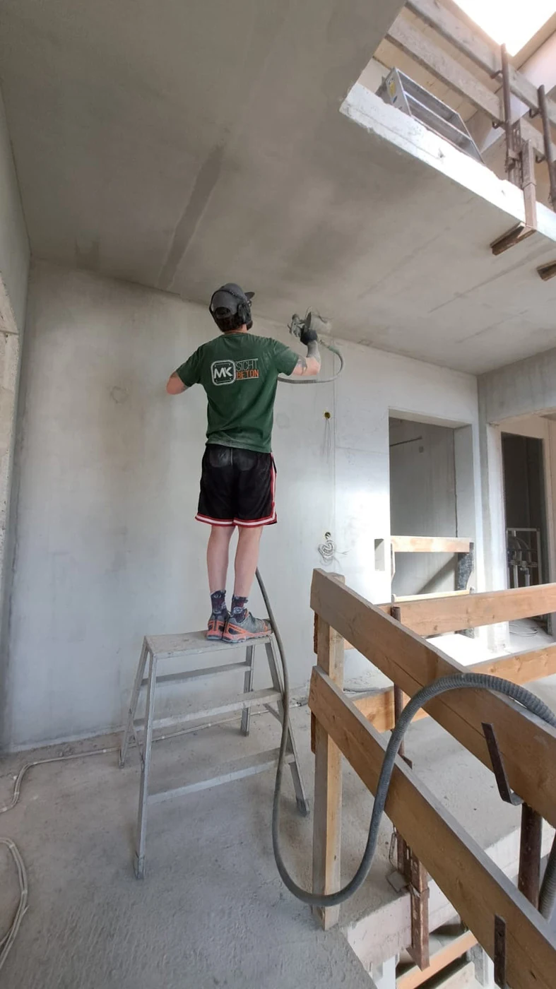 Handwerker auf der Stehleiter retuschiert eine Podestunterseite aus Betonfertigteil mit dem HVLP-Niederdruck-Spritzgerät