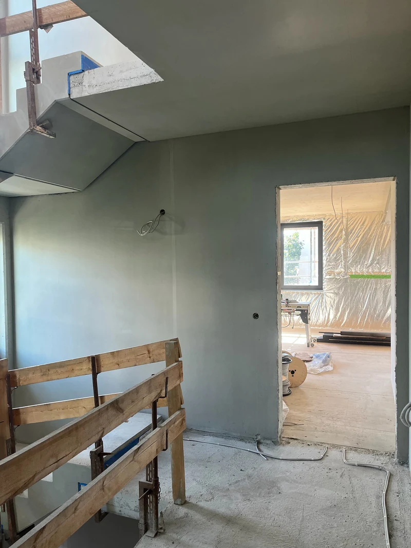 Nachher: Betonwand mit Durchgang und Holzgeländer, darüber eine retuschierte Podestunterseite, Rohbauphase