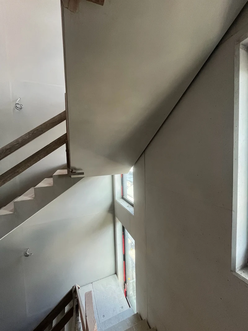 Nachher: Podestunterseite über einer Wand mit Fenstern, links das Holzgeländer, Treppenhaus in der Rohbauphase