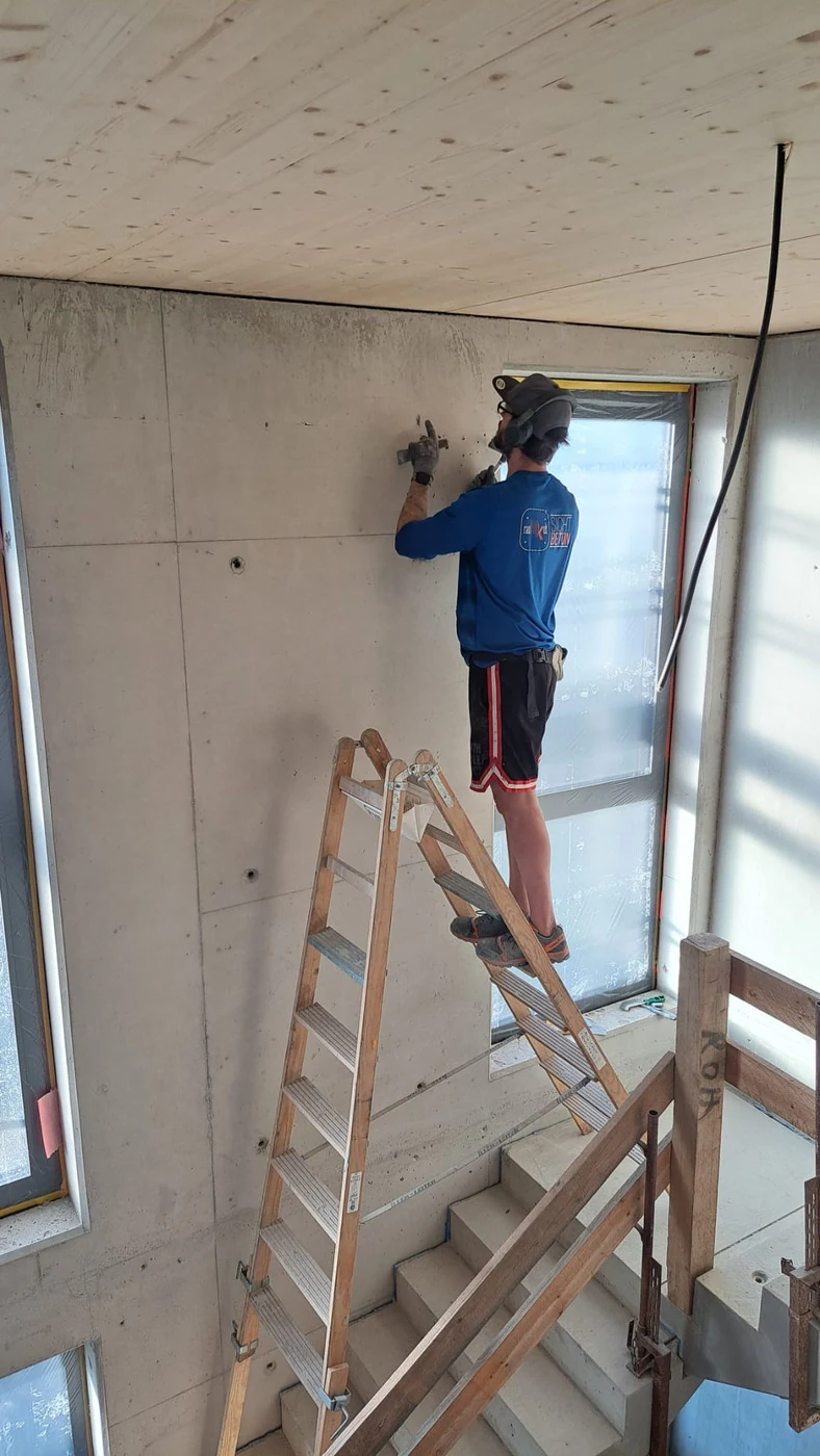 Ortbetonwand im Treppenhauskopf von links aufgenommen, ein Handwerker reinigt die Fläche in Wandhöhe von der Leiter aus