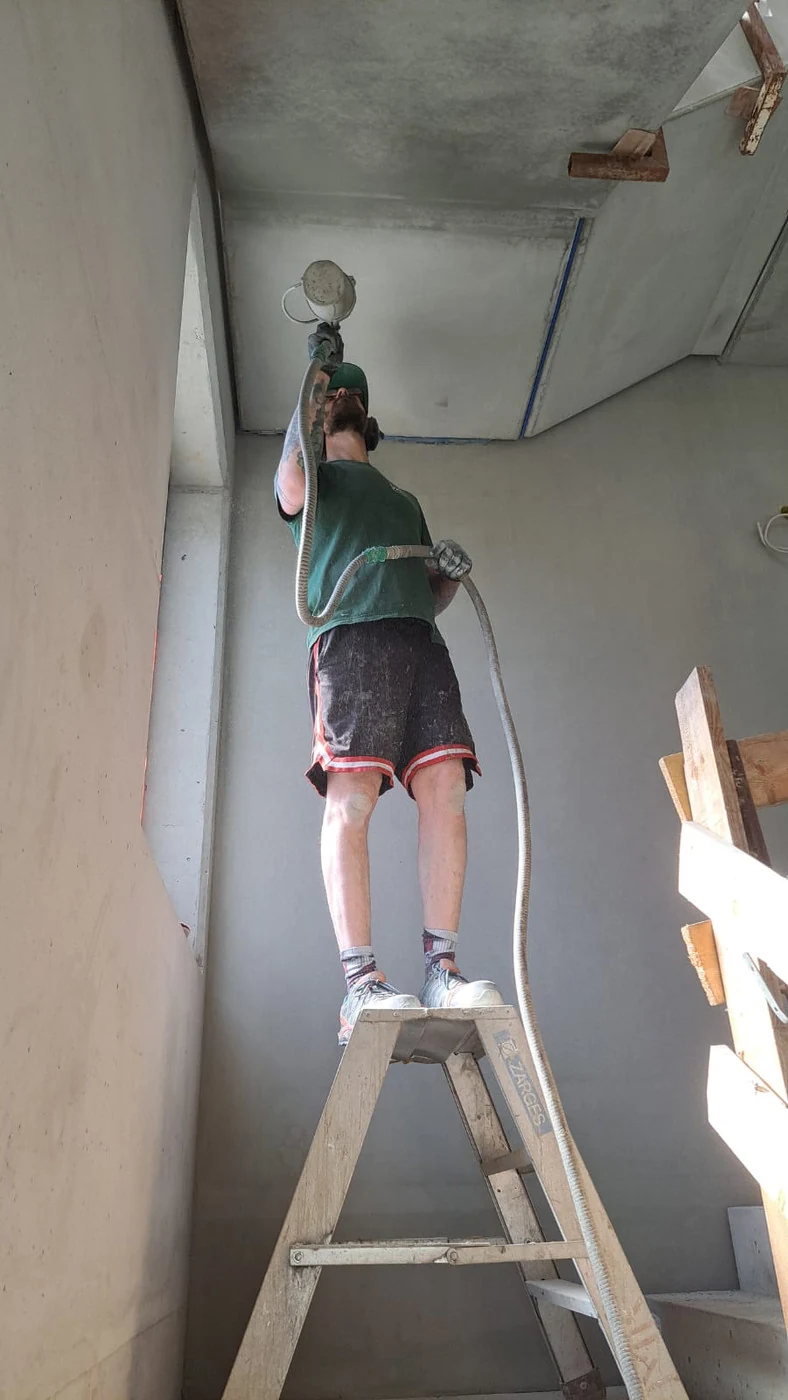 Retusche von Podestunterseite und Wand im Sichtbeton-Treppenhaus mit dem HVLP-Niederdruck-Spritzgerät von der Stehleiter