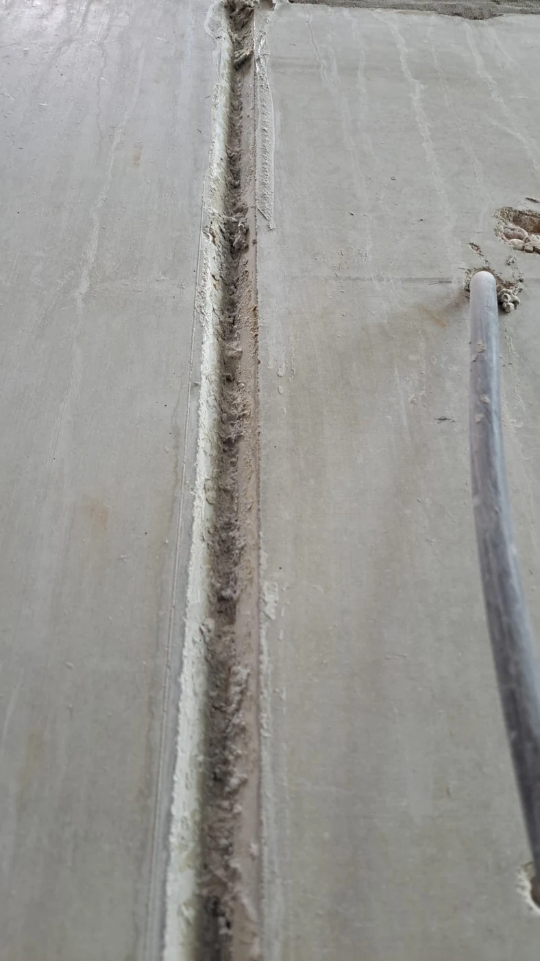 Vorher: lange senkrechte Betonfertigteilfuge im Treppenhaus, offen und mit Schmutz gefüllt, ein Kabel am Rand