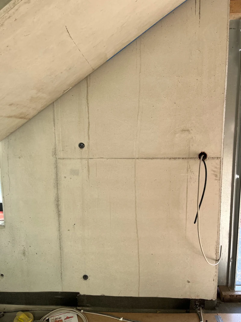 Vorher: Ortbetonwand aus Recyclingbeton unter dem Treppenlauf mit Verschmutzungen, Bohrlöchern und Kabeln